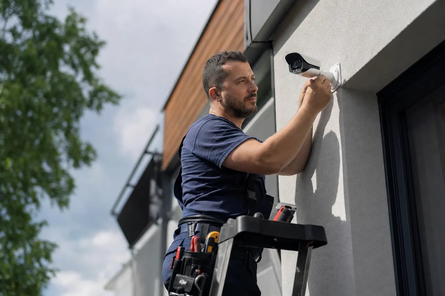 Security technician installing a surveillance camera on the exterior of a building while Callbook handles incoming alarm and assessment calls